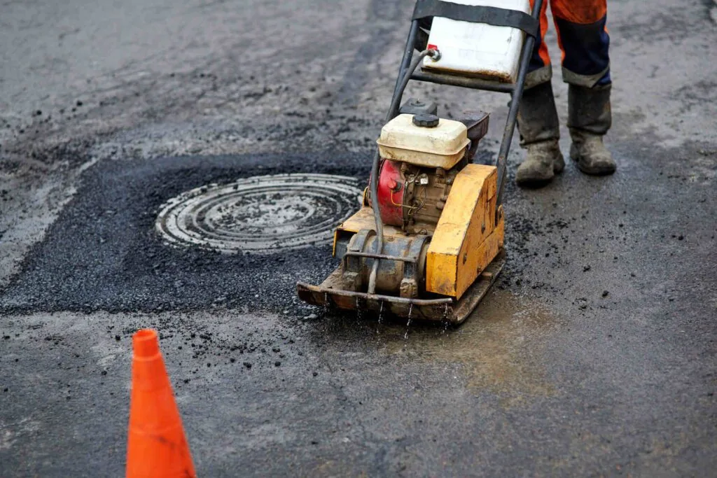 asphalt plate compactor fixing a patch with a manhole cover