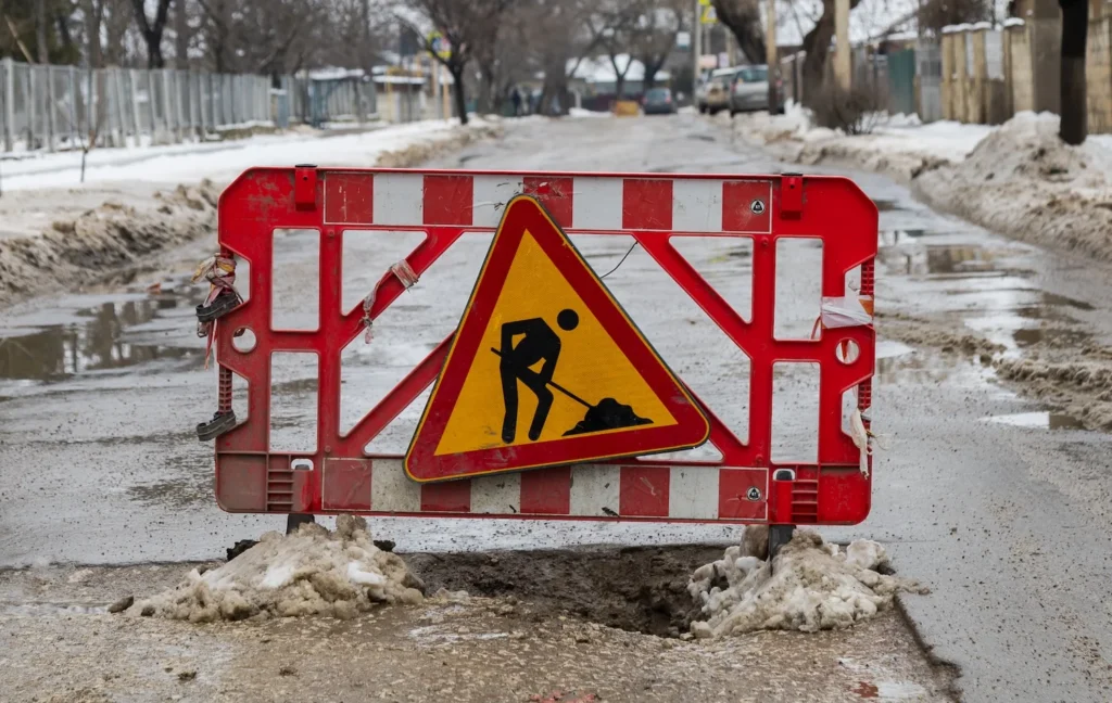 A red and white road work sign blocks a snowy street in a suburban neighborhood.